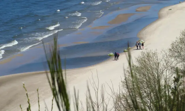 Plaża z falami, piaskiem i kilkoma spacerującymi osobami, widok z klifu.