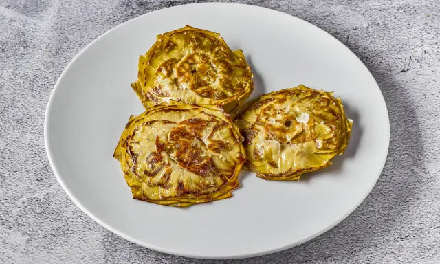 Tres alcachofas cortadas en rodajas, cocinadas a baja temperatura, con un toque de sal marina, servidas en un plato blanco.