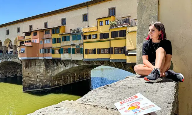 Ragazza seduta sul Ponte Vecchio, con la guida "Firenze cosa vedere in due giorni" a fianco.