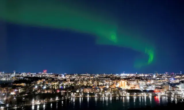 Grön norrsken dansar över ett upplyst Stockholm vid vatten.