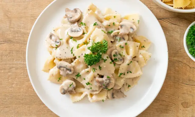 Szybki obiad z makaronem farfalle w kremowym sosie grzybowym, posypany natką pietruszki. Idealny na szybki posiłek.