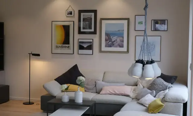 Przytulne mieszkania w Danii: salon z wygodną kanapą, galerią ścienną i designerską lampą.