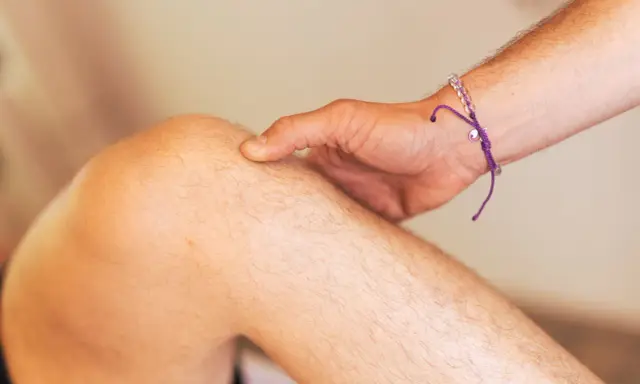 Ein Finger tastet das Knie ab, als ob ein Schleimbeutel im Knie geplatzt wäre.