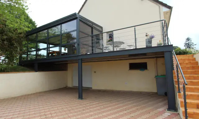 Modèle de véranda sur balcon avec structure métallique et vitrage. Un espace extérieur aménagé avec table et chaises.