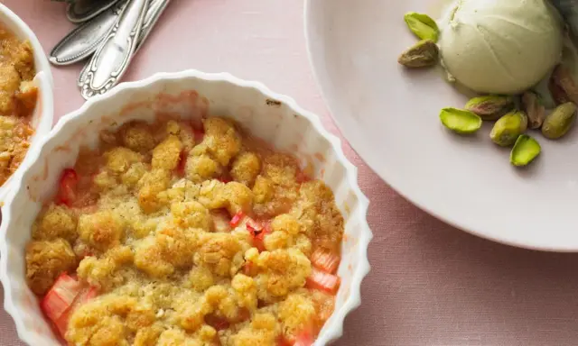Rhabarber-Crumble in weißer Auflaufform, daneben eine Kugel Eis mit Pistazien. Ein köstliches Rhabarber Dessert.