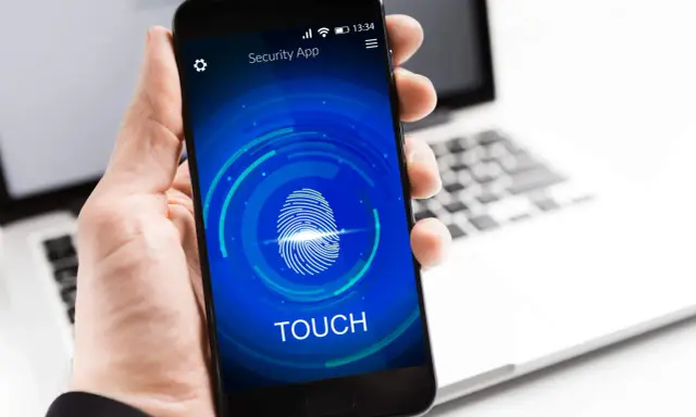 Dłoń trzyma smartfon z ekranem blokady "Security App" i ikoną odcisku palca. Proces autoryzacji jest w toku.