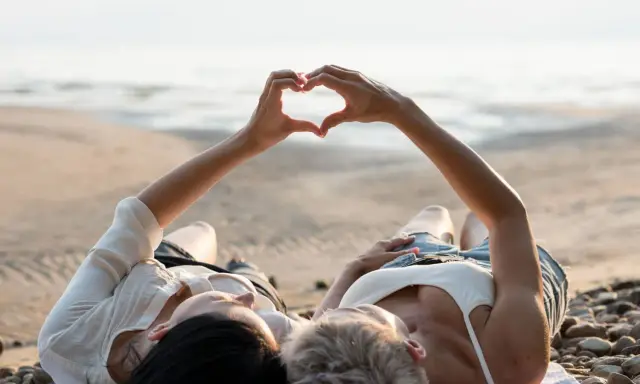 Para, które właśnie wzięło ślub, leży na plaży, tworząc serce dłońmi. Idealne miejsce na podróż poślubną.