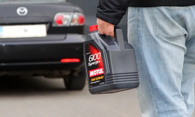 Mężczyzna niesie kanister z olejem silnikowym Motul, gotowy do recyklingu.