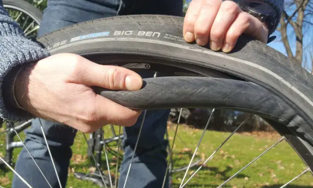 Hände wechseln einen platten Fahrradreifen. Der Reifen ist ein Schwalbe Big Ben.