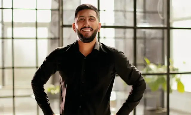 Man in zwart overhemd, handen in de zij, straalt zelfvertrouwen uit met een krachtige power pose.