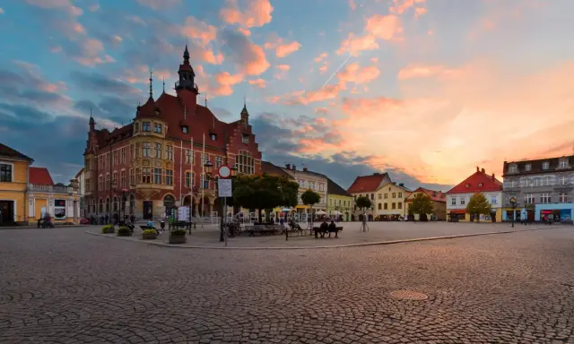 Rynek w Tarnowskich Górach o zachodzie słońca. Kolorowe chmury nad zabytkową zabudową i brukowanym placem, tworzą malownicze tarnowskie góry atrakcje.