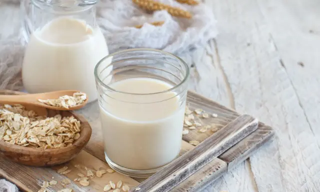 Szklanka i dzbanek z mlekiem owsianym, obok miseczka płatków owsianych. Idealne na zdrowe śniadanie, mleko 2 procent kcal.