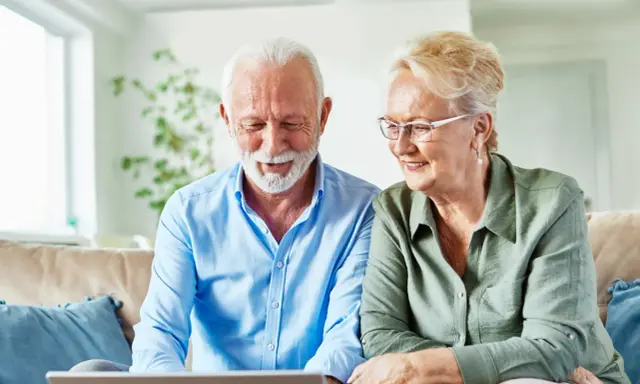 Uśmiechnięta para seniorów przegląda w internecie informacje, jak załatwiać sanatorium.