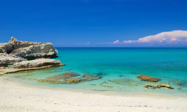 Spiaggia di Santa Domenica con rocce bianche e mare cristallino sotto un cielo azzurro.