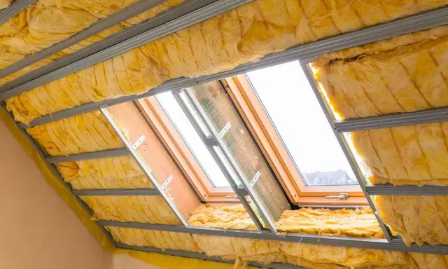 Travaux d'isolation toiture en cours. Laine de verre jaune installée entre les chevrons métalliques, autour de fenêtres de toit.