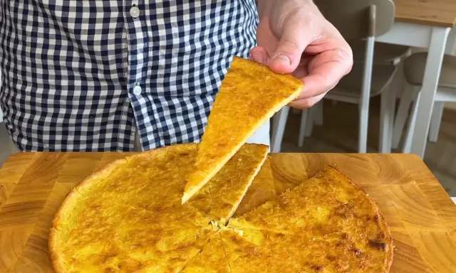 Una fetta di farinata di ceci dorata e croccante viene sollevata da una teglia rotonda su un tagliere di legno.
