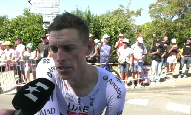 Brandon McNulty, Radfahrer im UAE-Trikot, gibt ein Interview. Im Hintergrund stehen Zuschauer und Straßenschilder.