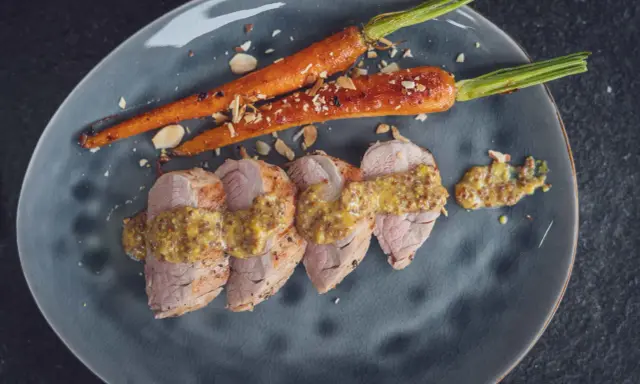 Zarte Scheiben von **schweinefilet grillen** mit Honig-Senf-Sauce und karamellisierten Karotten, bestreut mit Mandelsplittern.