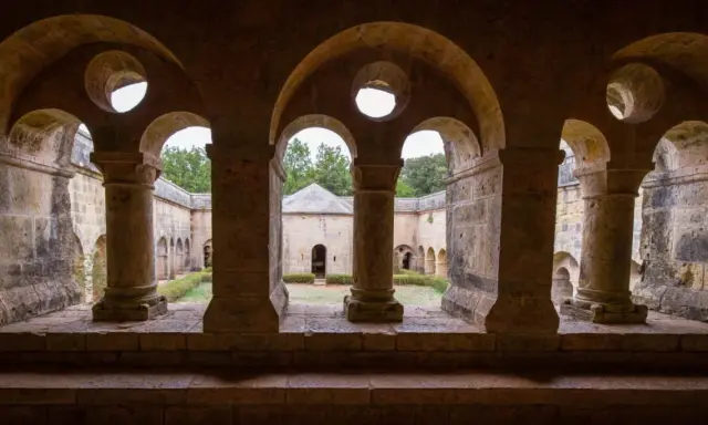 Vue à travers les arches de l'abbaye du Thoronet, un cloître en pierre avec un jardin verdoyant et des bâtiments anciens.
