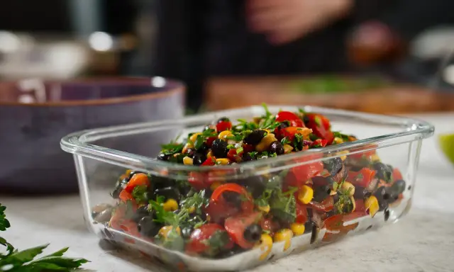 Frischer schwarze bohnen salat mit Mais, Tomaten und Kräutern in einer Glasbox.