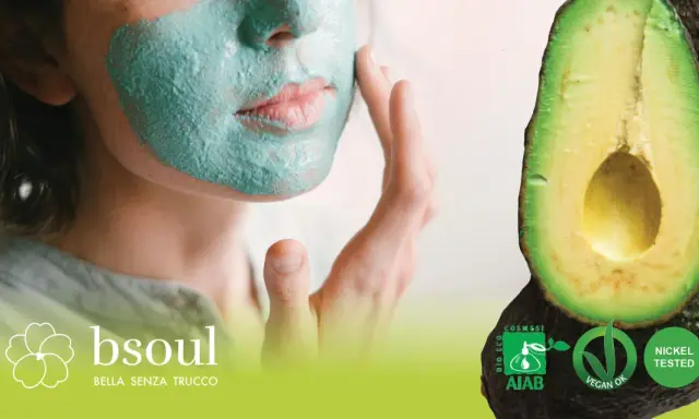 Donna con maschera viso fai da te verde, accanto ad avocado. Certificazioni bio e vegan.