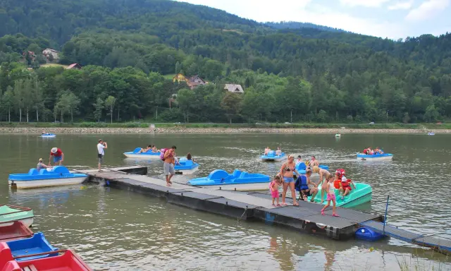 Wakacyjny dzień na Jeziorze Żywieckim. Ludzie pływają na rowerach wodnych, czując się jak na karaibskiej plaży.