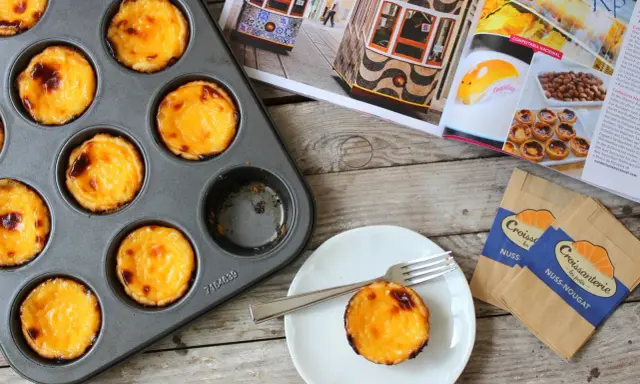 Pyszne, lekko przypieczone pastel de nata w blaszce i na talerzyku. Obok magazyn z widokiem na Lizbonę i tramwaje.