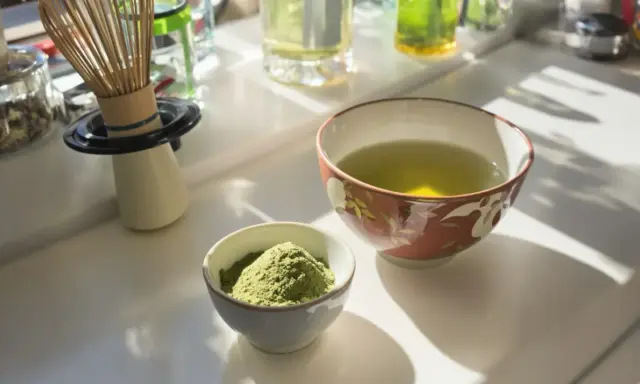 Zwei Schalen auf einem Tisch: eine mit grünem Pulver, die andere mit aufgebrühtem Sencha Tee. Die Wirkung von Sencha Tee ist belebend.