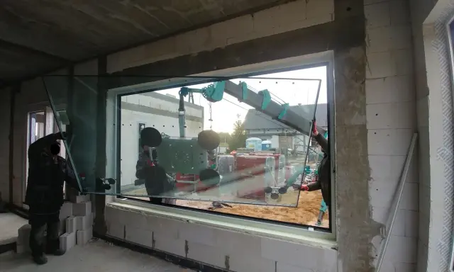 Pracownicy montują duże okno z użyciem dźwigu, zapewniając ciepły montaż okien.