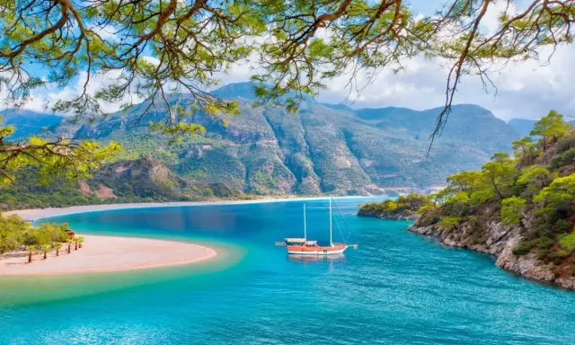 Malownicze widoki na turcja oludeniz: turkusowa woda, piaszczysta plaża i góry. Statek kołysze się na falach.