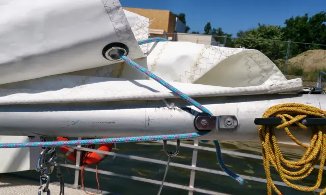 Poulie pour prise de ris automatique sur un mât de bateau, avec des cordages bleus et roses.