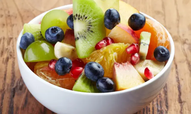 Kolorowa sałatka owocowa zimowa: kiwi, pomarańcza, winogrona, borówki, granat i brzoskwinia w białej misce.