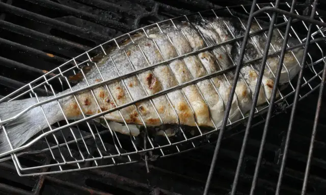 Ein ganzer Fisch wird in einem Grillkorb gegrillt. Die Haut ist goldbraun und leicht gebräunt.