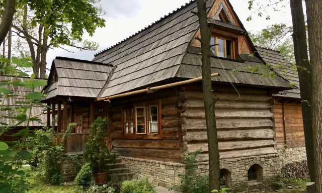 Drewniana chata z kamiennym fundamentem, kryta gontem, otoczona zielenią. Ulica Kościeliska w Zakopanem zachwyca tradycyjną architekturą.