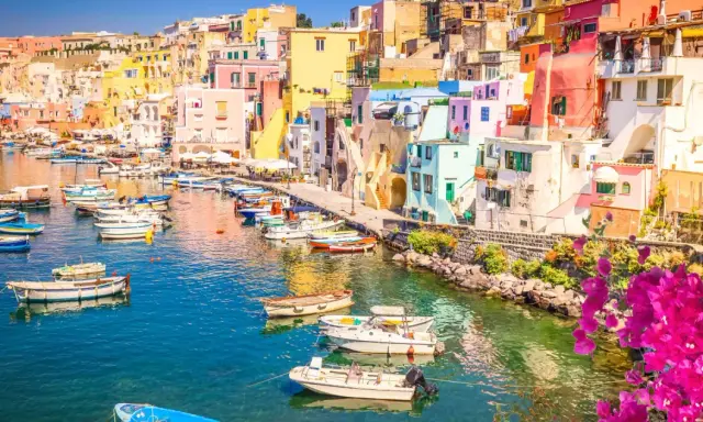Porto di Corricella a Procida, un gioiello colorato. Ecco cosa vedere a Procida in un giorno: case pastello, barche nel blu intenso e bouganville in fiore.