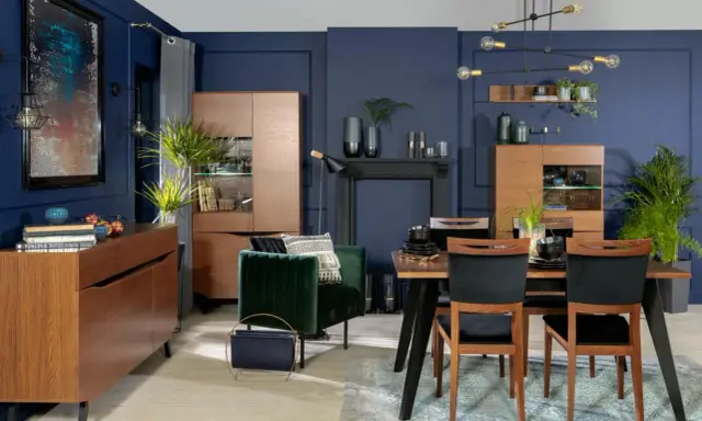 Inspiracje granatowa ściana w salonie: elegancka jadalnia z drewnianymi meblami, aksamitnym fotelem i nowoczesnym oświetleniem.