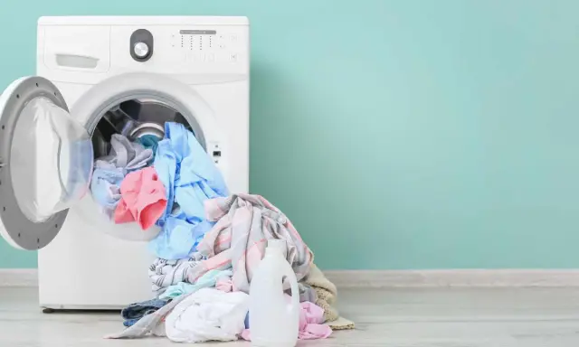 Lavadora blanca con ropa de colores y botella de detergente. Aprende como limpiar la lavadora para un mejor lavado.