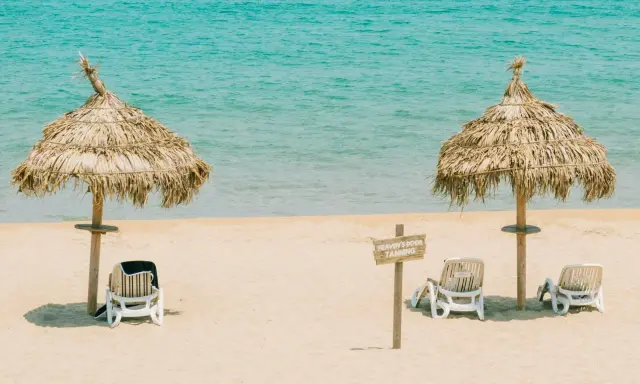Idealna pogoda Tunezja wrzesień: dwa słomiane parasole i leżaki na piaszczystej plaży, turkusowe morze w tle.