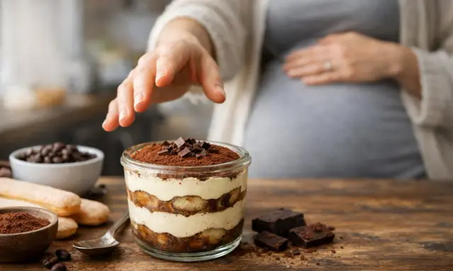 Une main effleure un tiramisu, un délice pour une femme enceinte. Le dessert, garni de cacao et de chocolat, promet un moment gourmand.