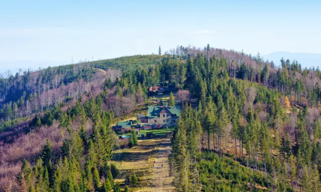 Widok na górskie schronisko na Babiej Górze, otoczone lasem iglastym i liściastym.