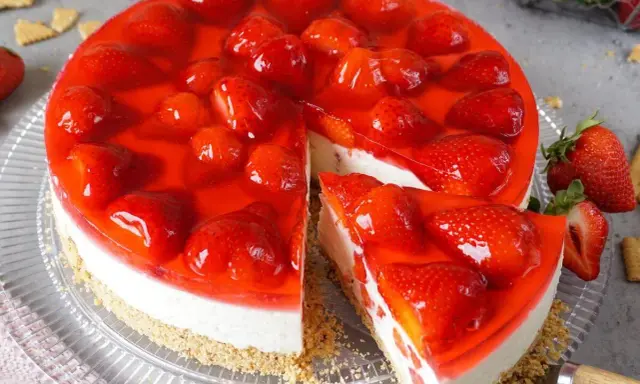 Ein saftiger erdbeerkuchen ohne backen mit frischen Erdbeeren und rotem Tortenguss. Ein Stück ist bereits angeschnitten.
