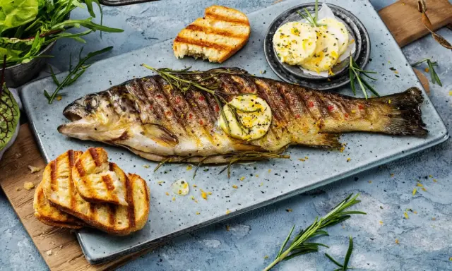 Perfekt gegrillte Forelle mit Kräutern, Zitronenscheibe und geröstetem Brot. Ein Genuss für jeden Fischliebhaber.