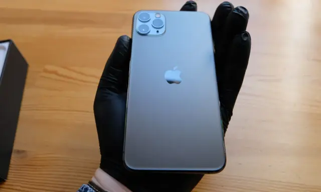 Ręka w czarnej rękawiczce trzyma elegancki iPhone 11 czarny. Obok leży czarne pudełko.