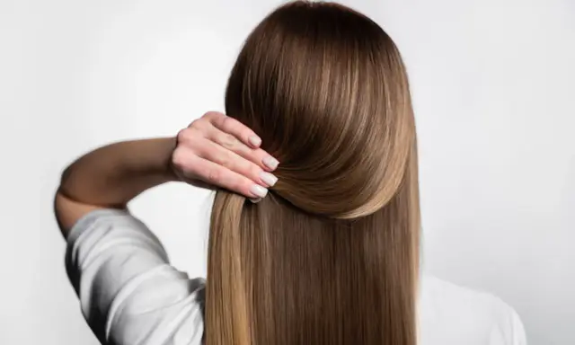 Capelli lisci e setosi, senza crespo, grazie a una routine efficace. La mano accarezza la chioma lucente.