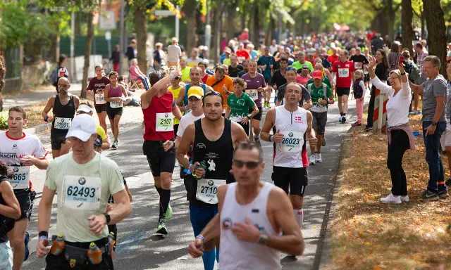 Läufer im Pulk auf einer Straße, einige mit Startnummern, die auf einen Marathon unter 4 Stunden hindeuten.