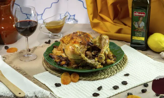 Pollo asado relleno, dorado y jugoso, servido en plato verde con pasas y orejones. Acompañado de vino tinto y aceite de oliva.