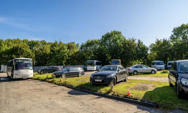 Na parkingu przy zamku Bolków stoi kilka samochodów i autobusów.