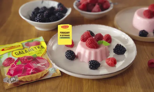 Panna cotta z malinami i jeżynami, obok opakowanie galaretki malinowej.