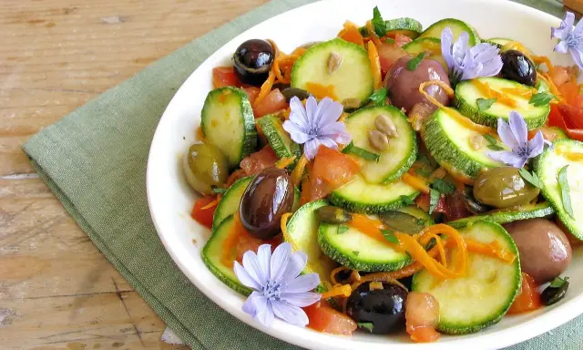Insalata di zucchine fresca con pomodori, olive, carote e fiori di cicoria, un piatto colorato e leggero.