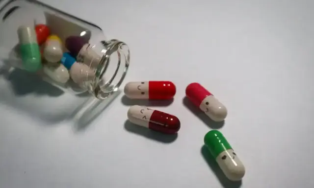 Kolorowe kapsułki, niektóre z uśmiechniętymi buźkami, wypadają z butelki. To mogą być psychotropy, które pomagają w trudnych chwilach.